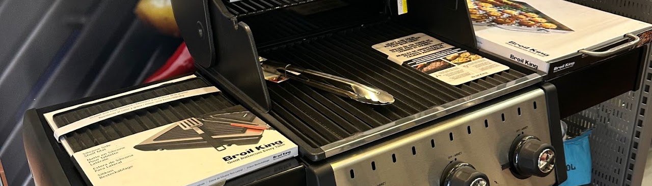 Broil King gasolgrill med uppfällt lock och en grilltång på gallret inne i butiken