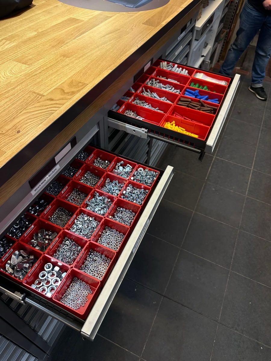 Utdragna butikslådor med röda fack fulla av muttrar, brickor och plugg under en ekdisk