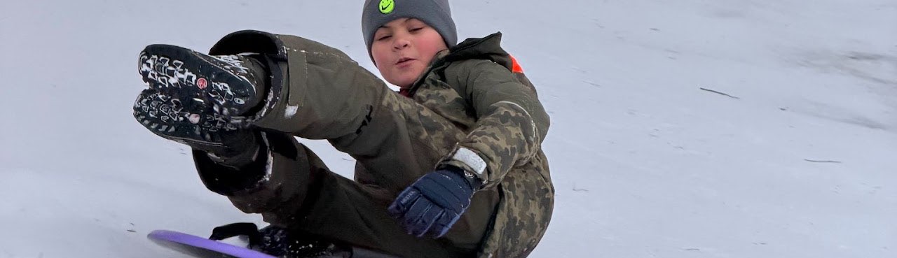 Barn i vinteroverall åker nedför en snöig backe på en lila plastpulka